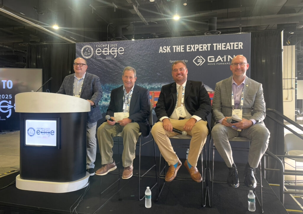 Four men seated on a conference stage.
